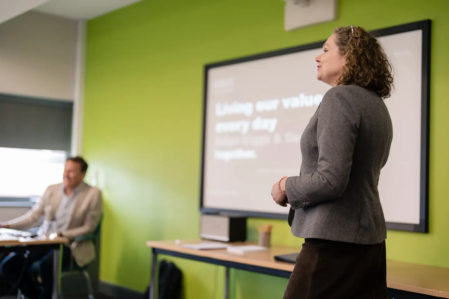 Kirsty Goddard standing to present to a room, a slide reading 'Living our values every day' on the screen behind her